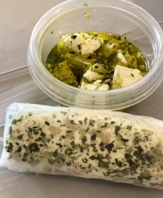 A roll of herbed goat cheese and a tub of marinated Feta cheese, both homemade.