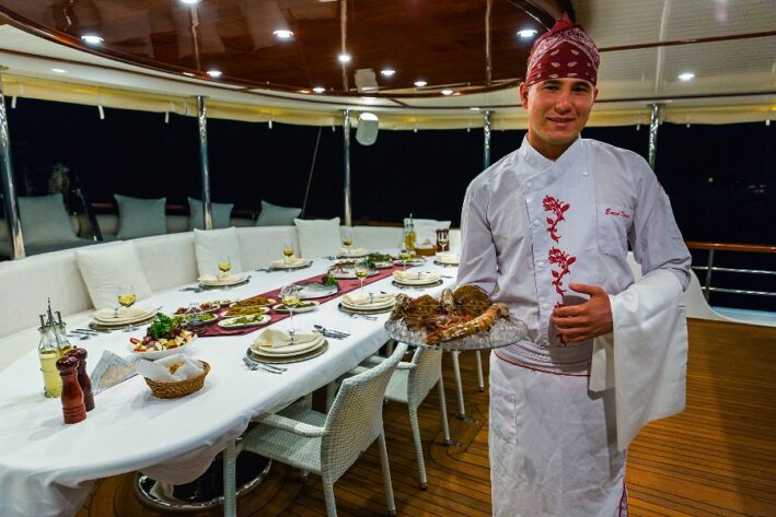 A chef holds a plate of food on a Turkish gulet cruise.