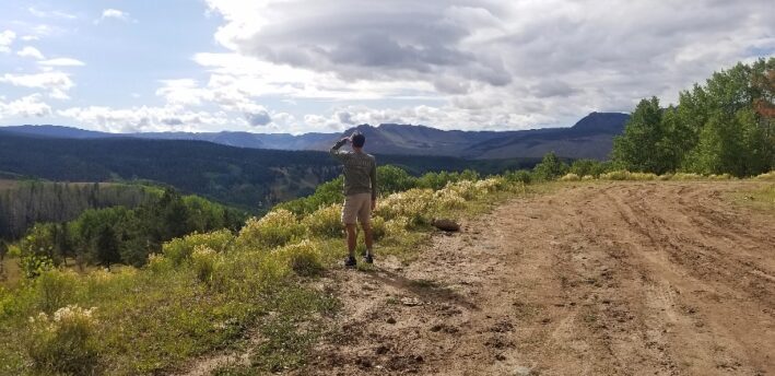 Man standing between dirt road and mountainside
