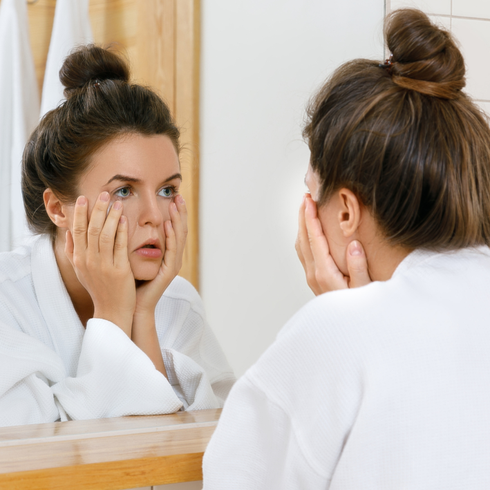 Woman looking in the mirror unhappy with how she looks.