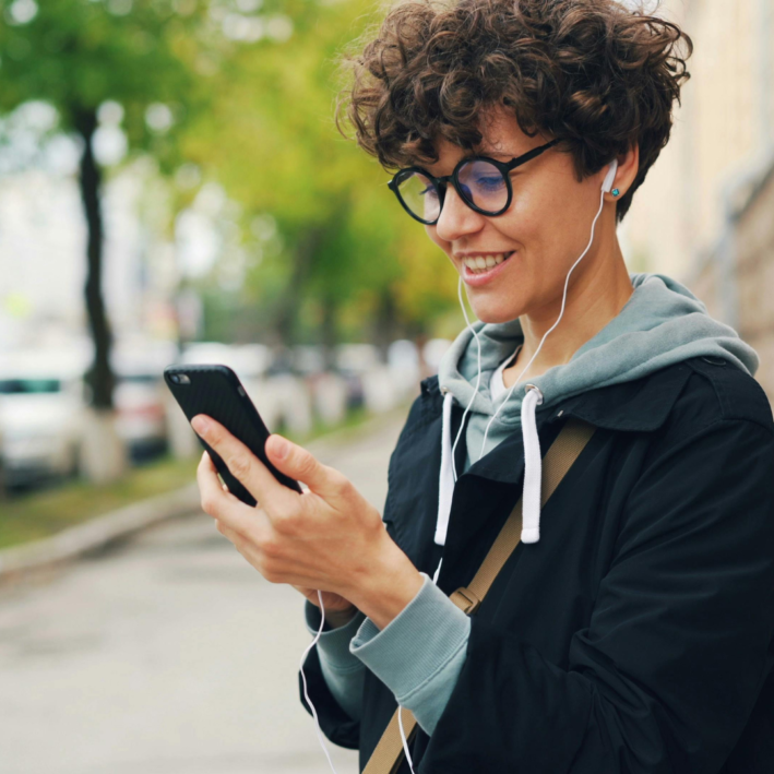 Person with curly hair and glasses using cell phone.